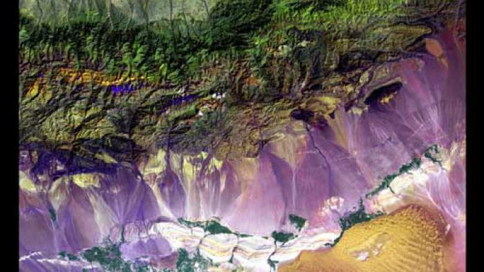 The Bogda Mountains next to the Turpan Depression. Green mountainous terrain at the top of the image. The bottom of the image is purple with a yellow spot on the right side. Groupings of green dots can be seen in the bottom of the image.